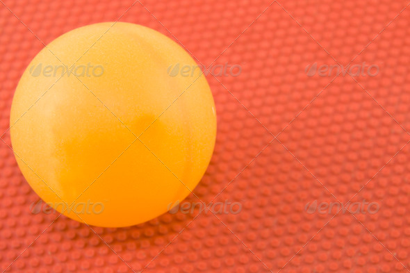 closeup of orange ping pong ball on red textured paddle