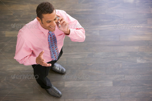 Businessman standing indoors using cellular phone smiling - Stock Photo - Images