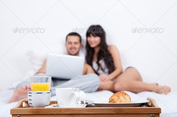 Young couple lying up in bed with laptop - Stock Photo - Images