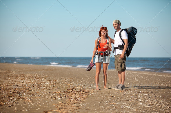 couple with backpacks walking on sea shore - Stock Photo - Images