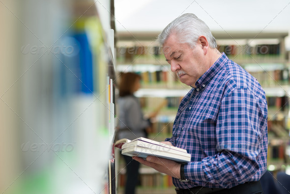 old man reading and choosing book in library - Stock Photo - Images