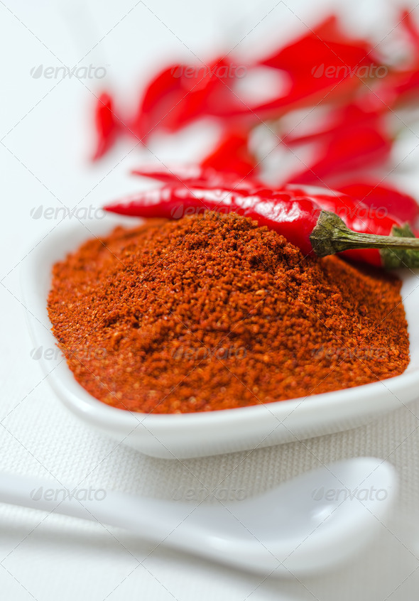 Ground cayenne pepper with whole peppers against a white canvas background.