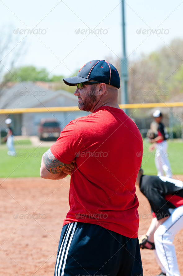 Baseball coach at first base line looking at batter.