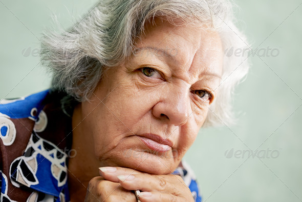 Portrait of serious old woman looking at camera with hands on ch - Stock Photo - Images