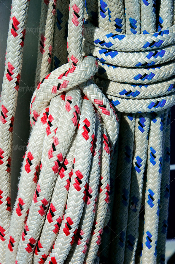 A photo of blue and red boat ropes hanging from a yacht mast