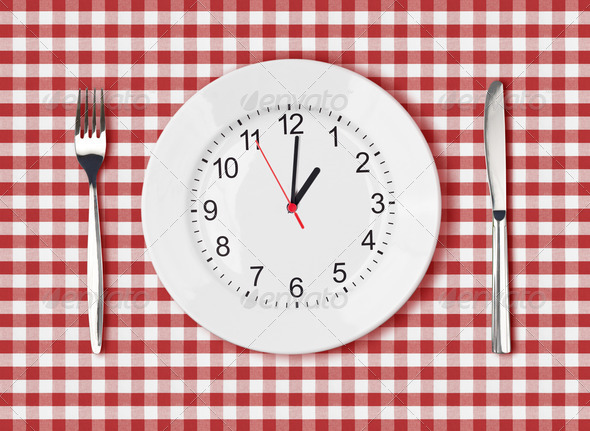 Knife, white plate with clock face and fork on red picnic table cloth