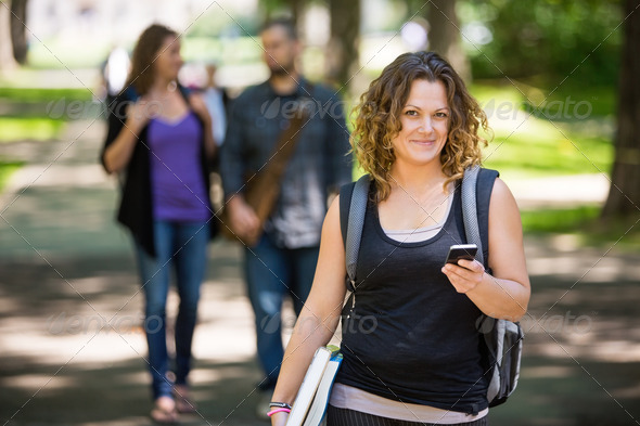 Portrait of female student with backpack holding cellphone while standing on campus