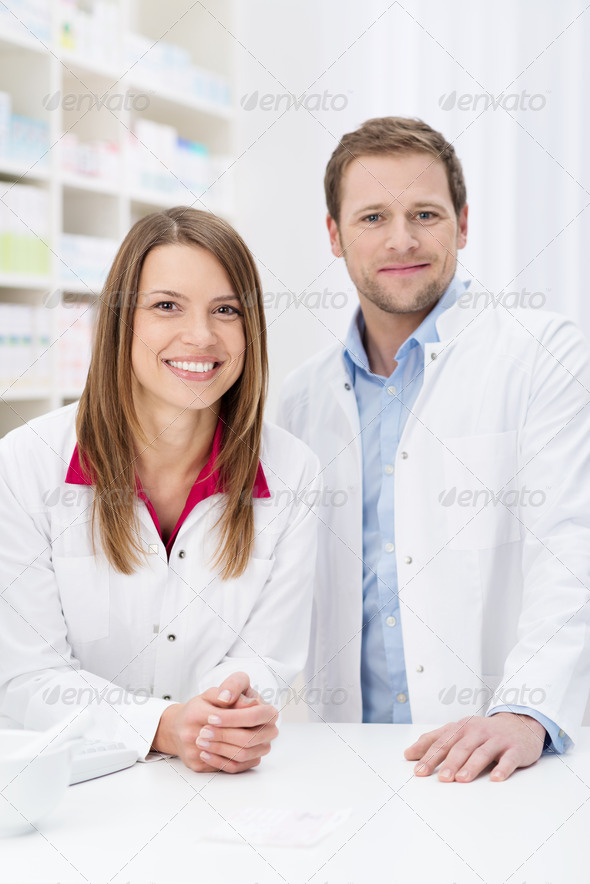 Successful pharmacy partnership with a confident young male and female pharmacist standing close together behind the counter in the pharmacy smiling at the camera