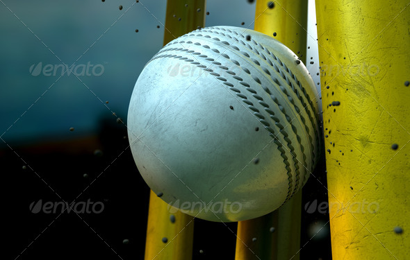 A white leather stitched cricket ball hitting yellow wooden wickets with dirt particles emanating from the impact at night