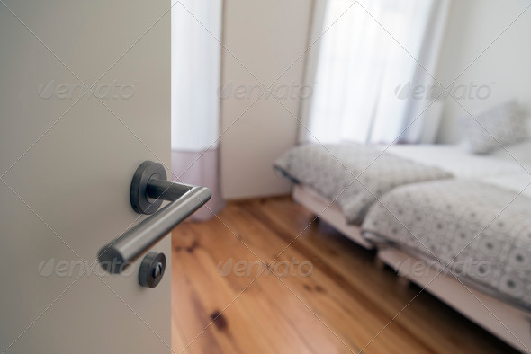 door handle in focus. Door opens to show modern bedroom defocussed in background