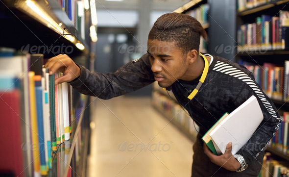 Young student finding reference books in university library. Finding information for his studies.