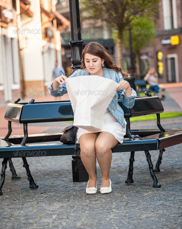 woman sitting on bench and looking inside of white paper bag aft (Misc) Photo Download