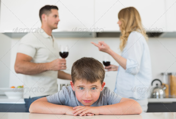 Portrait of sad boy leaning on table while parents arguing in background at home (Misc) Photo Download