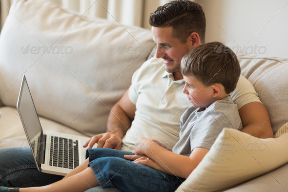 Father and son using laptop while relaxing on sofa at home (Misc) Photo Download