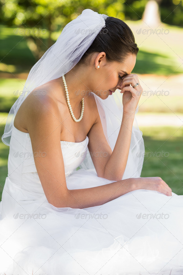 Side view of a beautiful worried bride sitting at the park (Misc) Photo Download