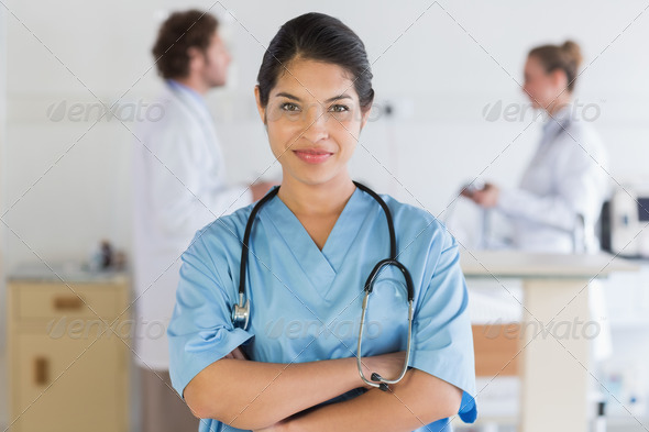 Portrait of confident female nurse with doctors in background at hospital (Misc) Photo Download