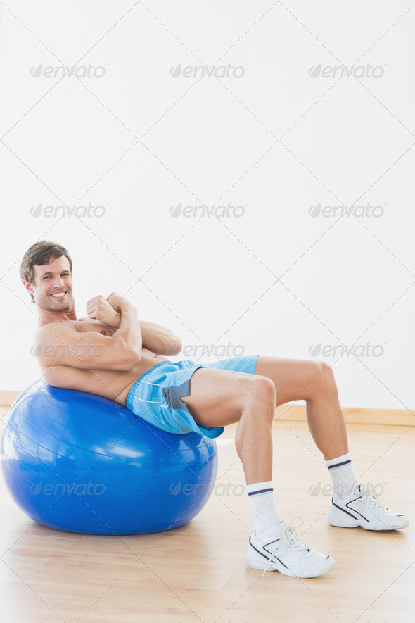 Full length of a shirtless man exercising on fitness ball in the gym (Misc) Photo Download