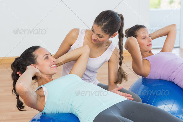 View of a trainer helping young woman with fitness ball at a bright gym (Misc) Photo Download