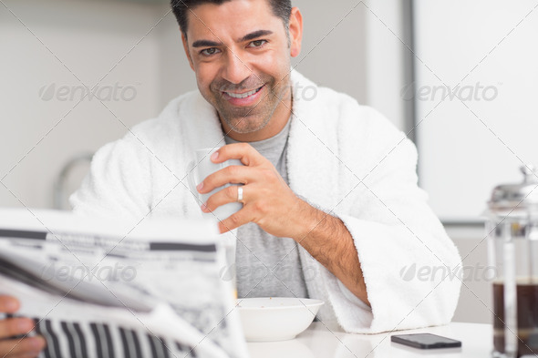 Portrait of a smiling casual man with coffee cup reading newspaper in the kitchen at home (Misc) Photo Download