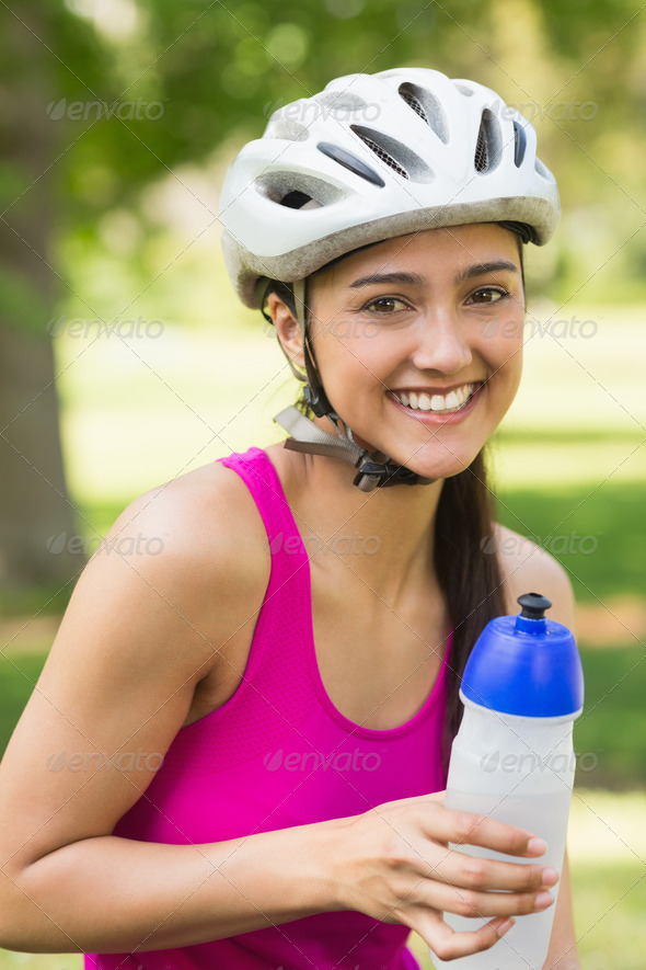 Portrait of a fit young woman in helmet holding water bottle at the park (Misc) Photo Download