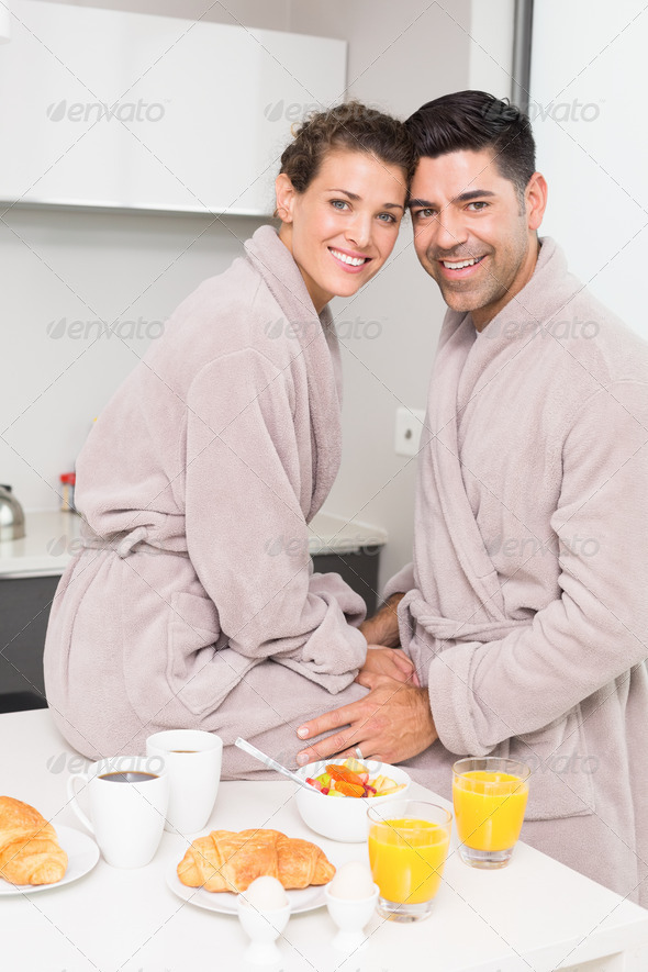 Smiling couple in bathrobes having breakfast together at home in kitchen (Misc) Photo Download