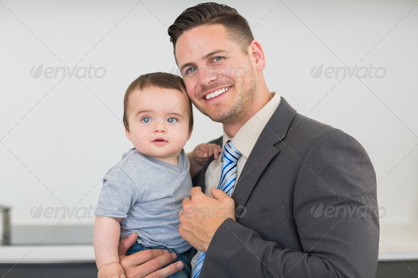 Portrait of smart businessman carrying baby boy in kitchen at home (Misc) Photo Download