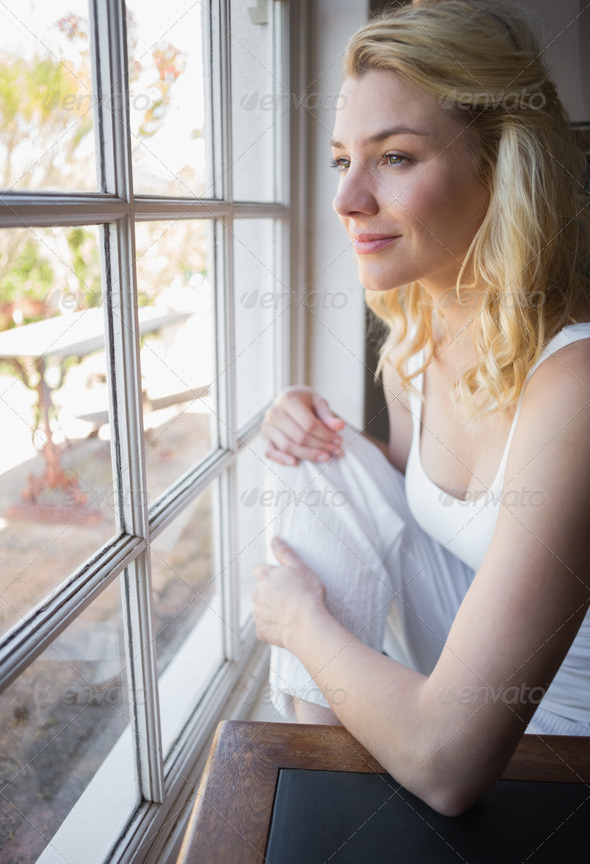 Pretty blonde looking out the window at home in the living room (Misc) Photo Download