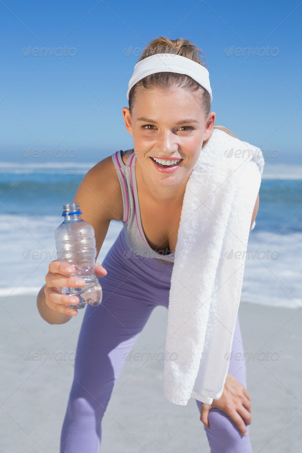 Sporty smiling blonde standing on the beach with towel and bottle on a sunny day (Misc) Photo Download