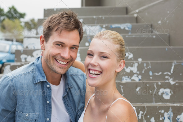 Hip young couple sitting on steps smiling at camera on a sunny day in the city (Misc) Photo Download