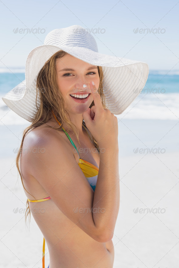 Beautiful girl putting spf on nose on the beach smiling at camera on a sunny day (Misc) Photo Download