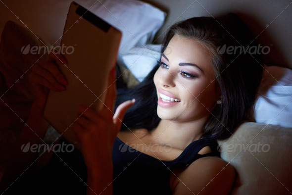 Smiling woman in bed reading a tablet at night