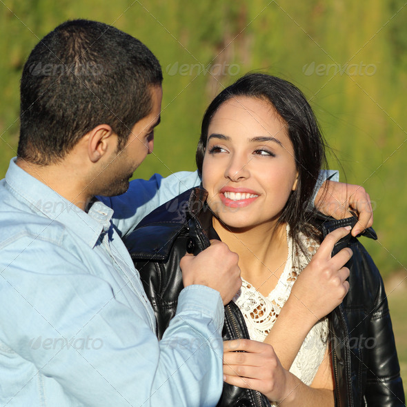 Happy arab couple flirting while man cover her with his jacket in a park