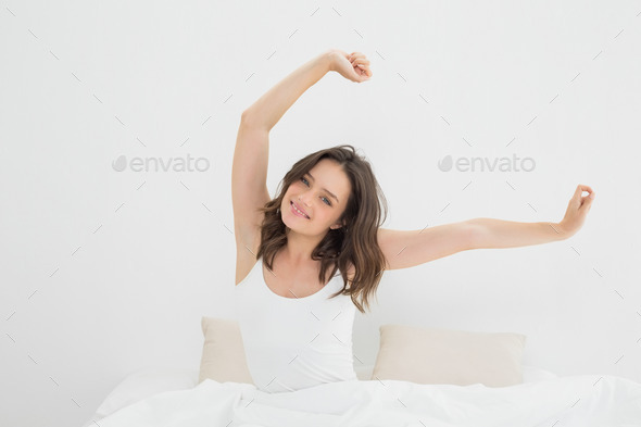Portrait of a smiling young woman waking up in bed and stretching her arms