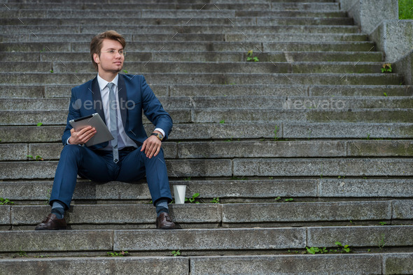 Confident businessman in glasses sitting on the steps and work o