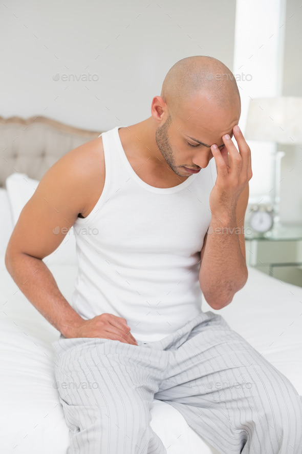 Young bald man suffering from headache in bed at home