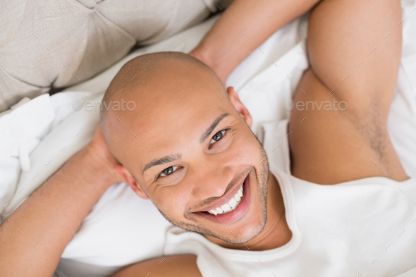 Close up portrait of a smiling young bald man resting in bed at home