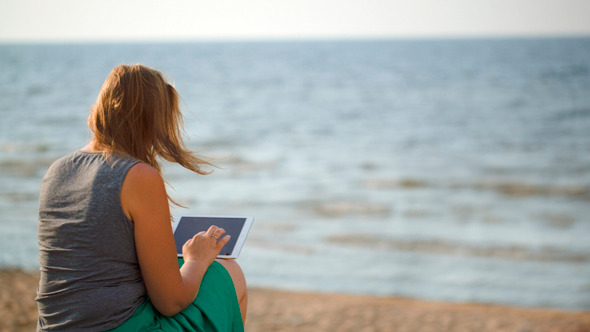 Woman Sitting On Beach By The Sea With Touch Pad Woman Sitting On Beach By The Sea With Touch Pad