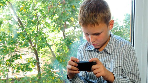 Boy Sitting By A Window Using His Smartphone Boy Sitting By A Window Using His Smartphone