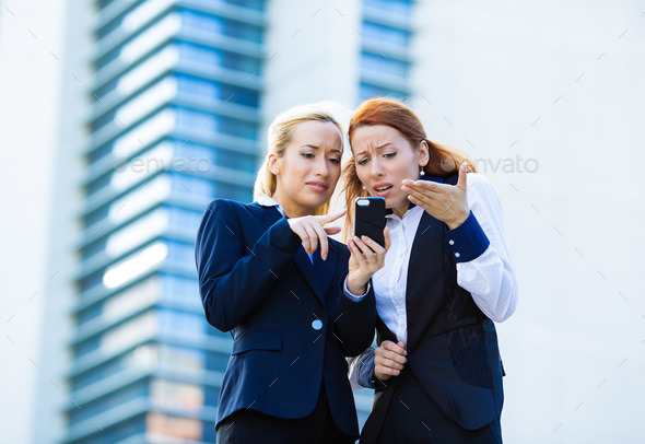 Two unhappy women reading news on smartphone