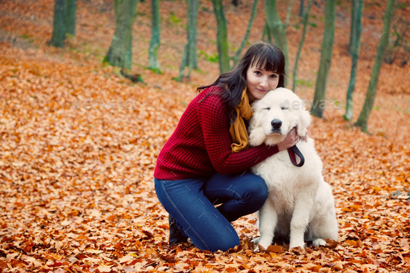 Young pretty woman hugging cute white puppy dog in autumn fall park.