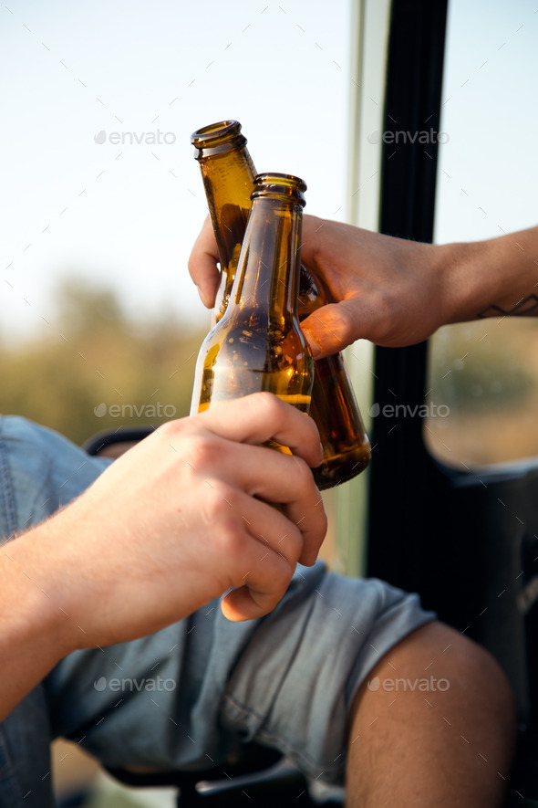 Portrait of two friends toasting with bottles of beer in car.