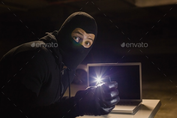 Robber looking at camera while making light with his phone on black background (Misc) Photo Download