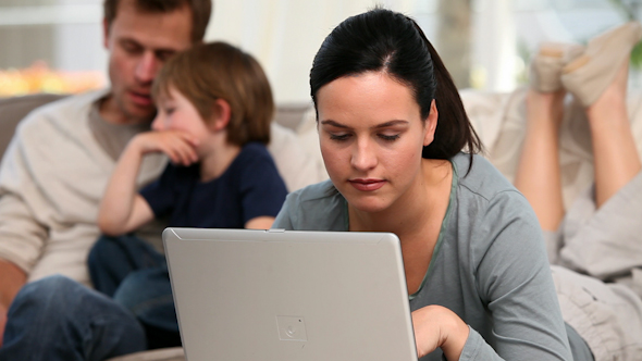 Beautiful Woman Is On Her Laptop While Her Family Is On A Sofa Beautiful Woman Is On Her Laptop While Her Family Is On A Sofa