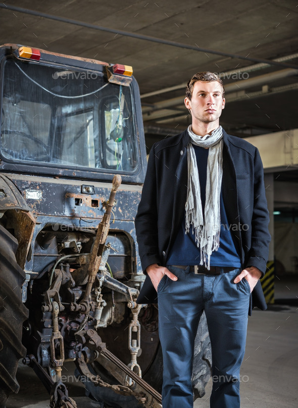 Fashion shot: handsome young man wearing jeans and coat against the tractor (Misc) Photo Download