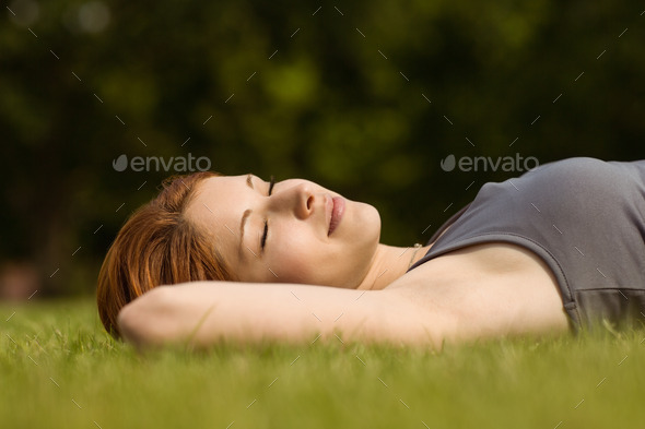 Pretty redhead lying with her eyes closed in park at sunshine (Misc) Photo Download