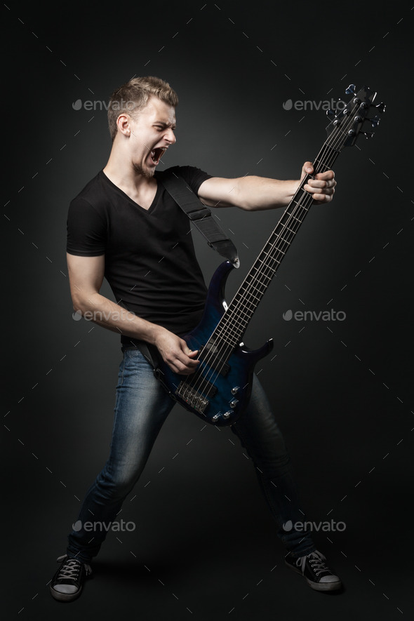 young male musician playing a six-string bass guitar isolated on dark background