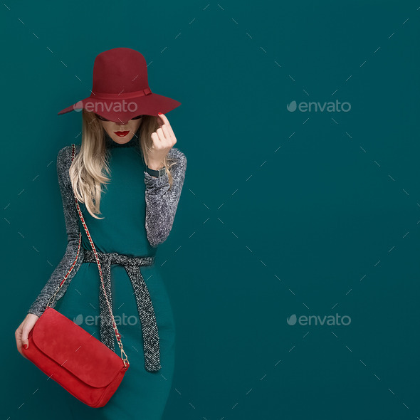 Lovely blond model in fashionable red hat and a red clutch on gr
