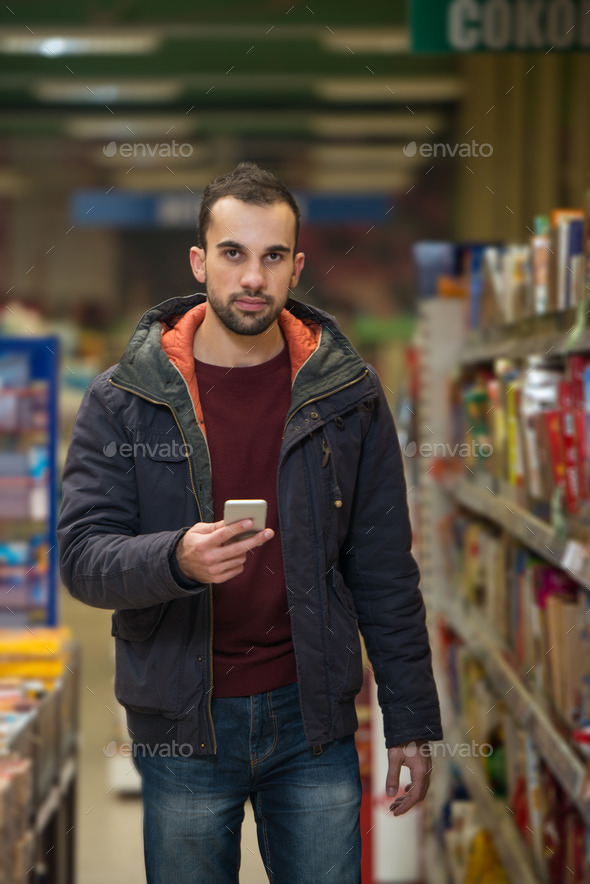 Young Man Typing On Mobile Phone At Supermarket