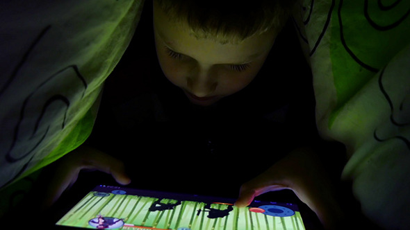 Young Boy Uses A Digital Tablet Under The Covers Young Boy Uses A Digital Tablet Under The Covers