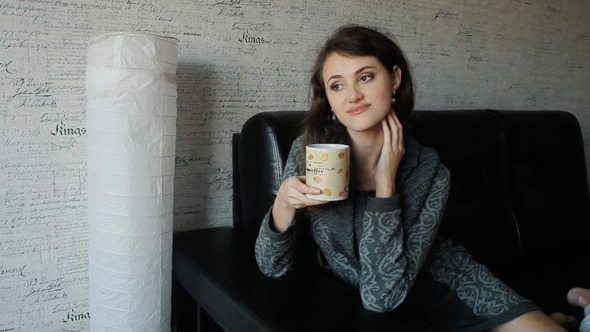 Young Woman Sitting On Sofa Drinking Tea Or Coffee Young Woman Sitting On Sofa Drinking Tea Or Coffee